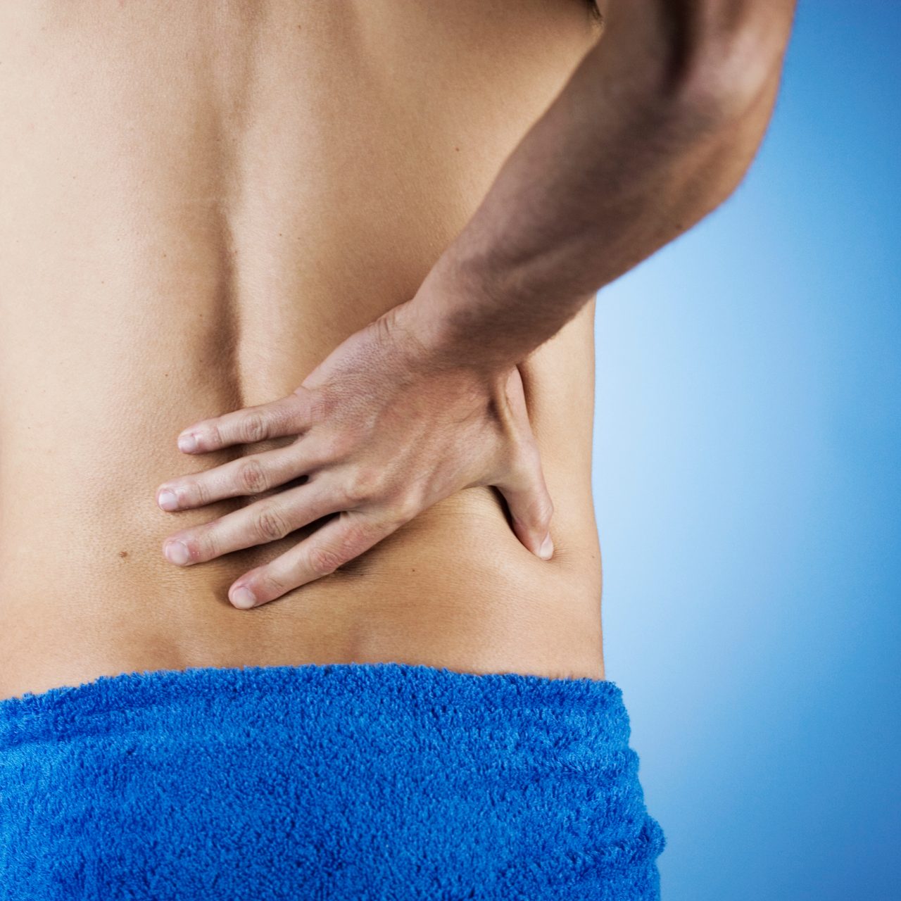 An adult man holding his back in discomfort.