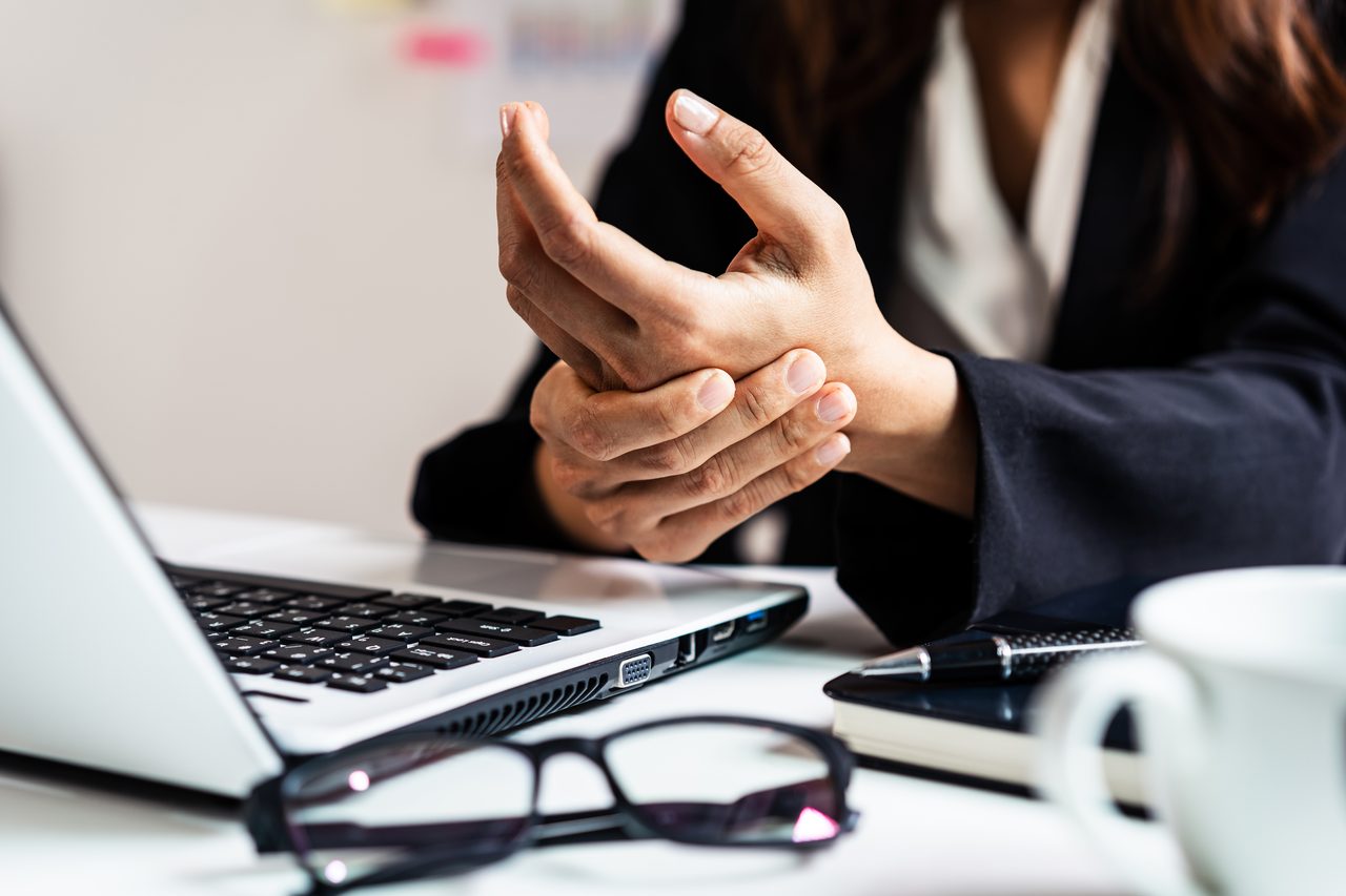 A business worker holding her wrist in discomfort at a desk.
