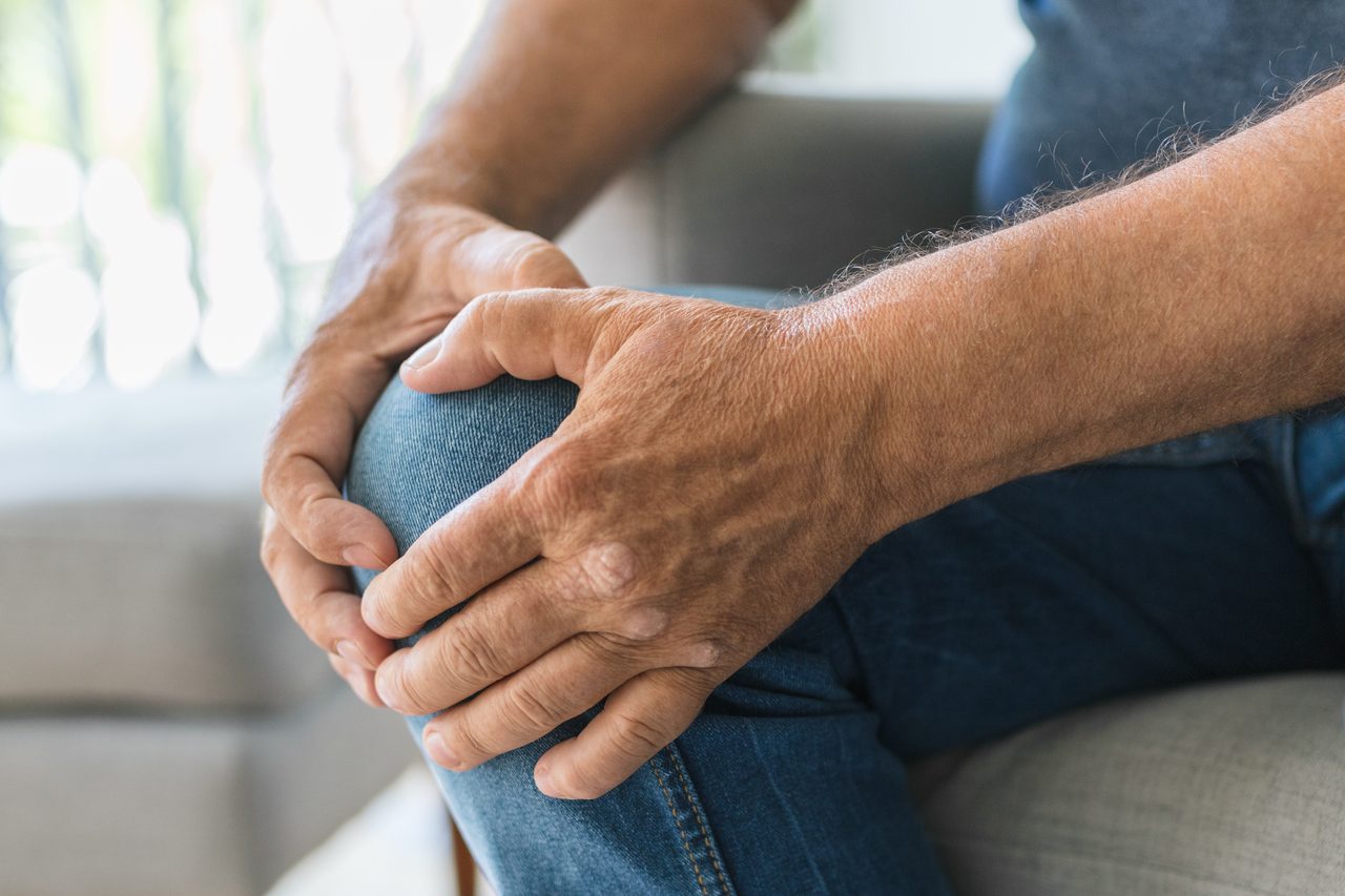 Older hands resting on a knee in a quiet indoor setting.