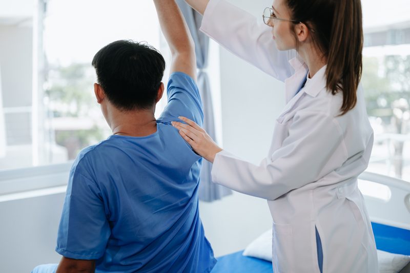A doctor assisting a patient with an arm-raise exercise.