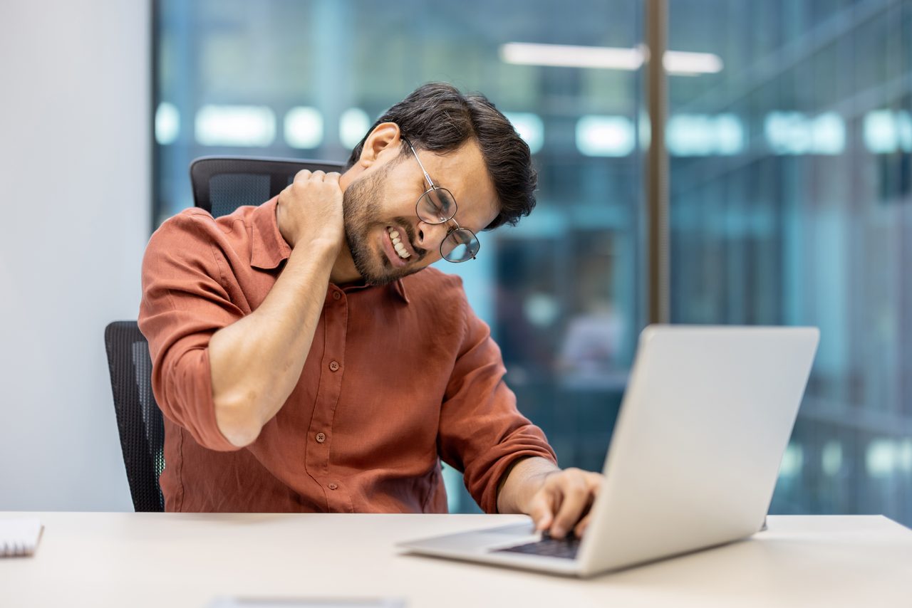 A stressed office worker holding their neck at a laptop.